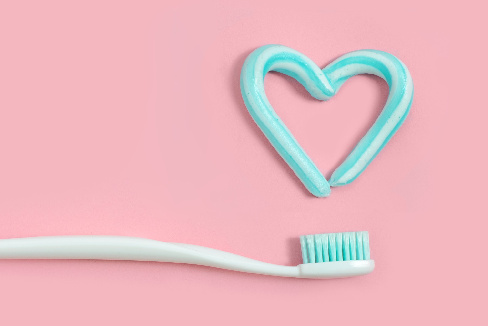 A toothbrush next to a swirl of white and blue toothpaste in the shape of a heart
