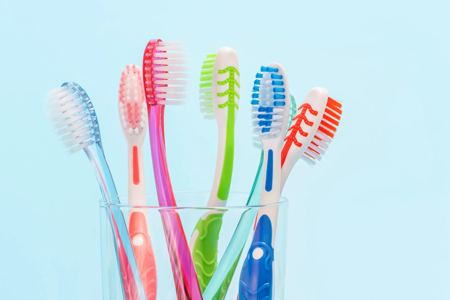Several colourful manual toothbrushes in a clear glass