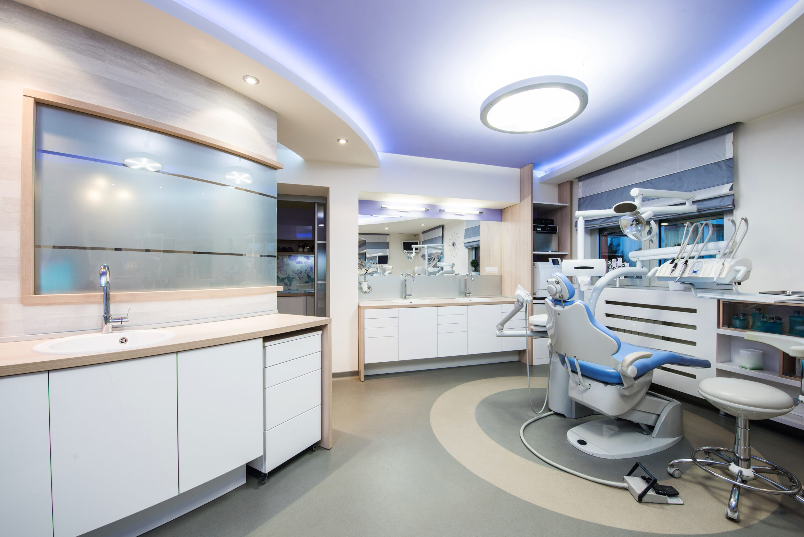 Modern dental operatory room with a patient chair, blue ambient lighting and white cabinetry