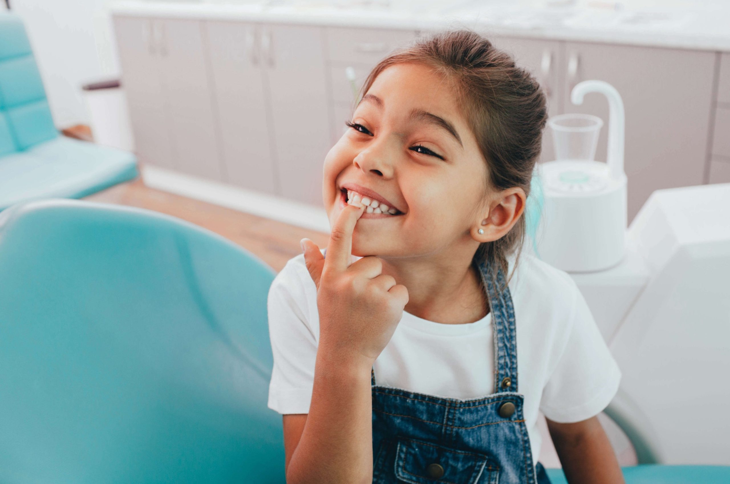 Happy girl pointing at teeth in dental chair