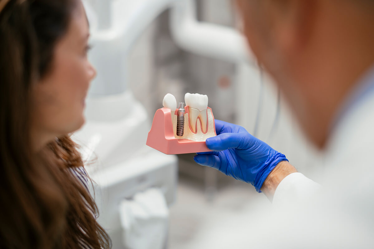 Dentist showing a dental implant model to a patient during a consultation.
