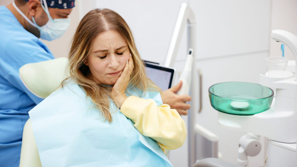 Patient experiencing tooth pain while sitting in a dental chair during treatment.