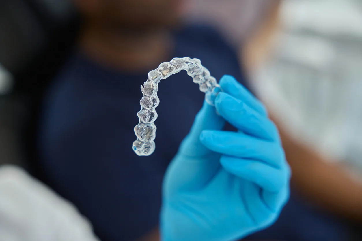 Sterile gloved hand holding an Invisalign clear aligner ready for placement