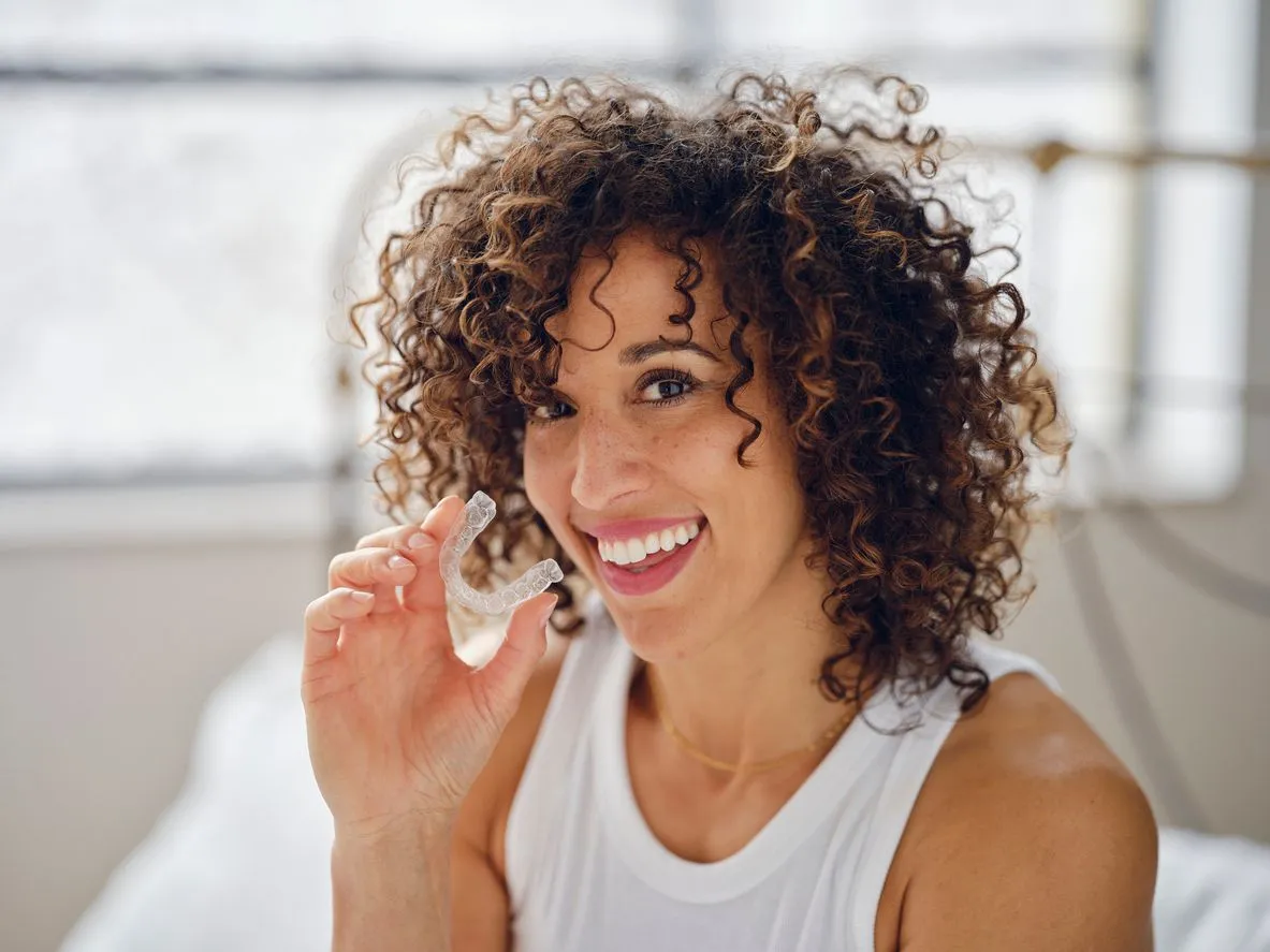 Woman smiling while holding Invisalign clear aligners in her hand