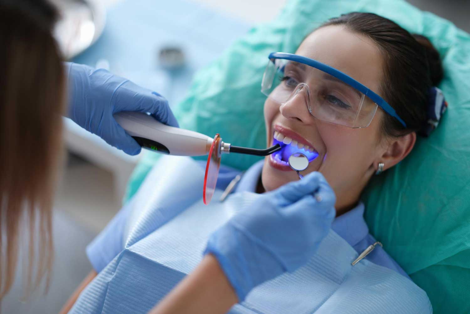 Dentist using a curing light to harden composite bonding on a patient’s teeth