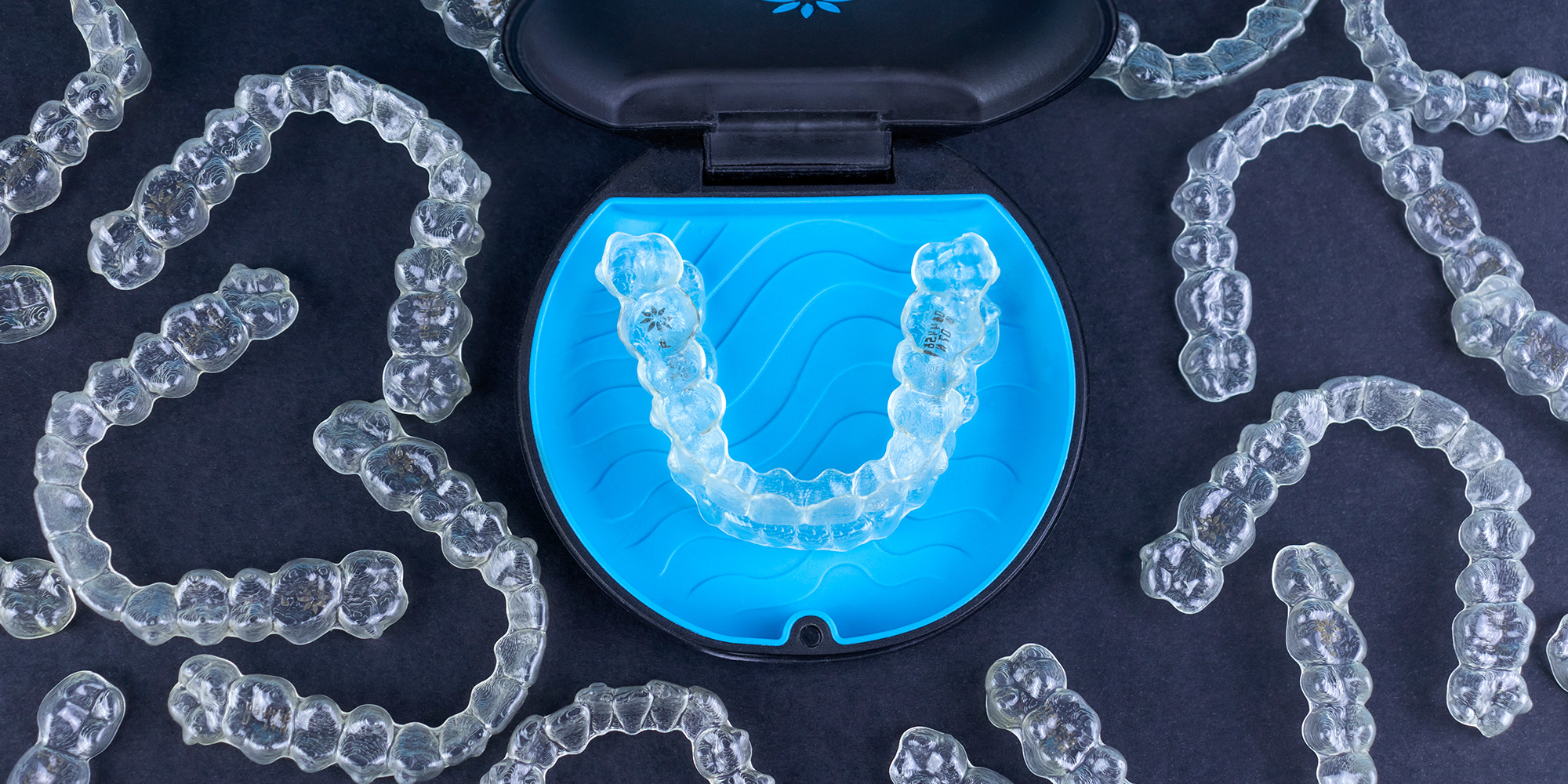 Several Invisalign moulds arranged on a black table with a blue case in the center