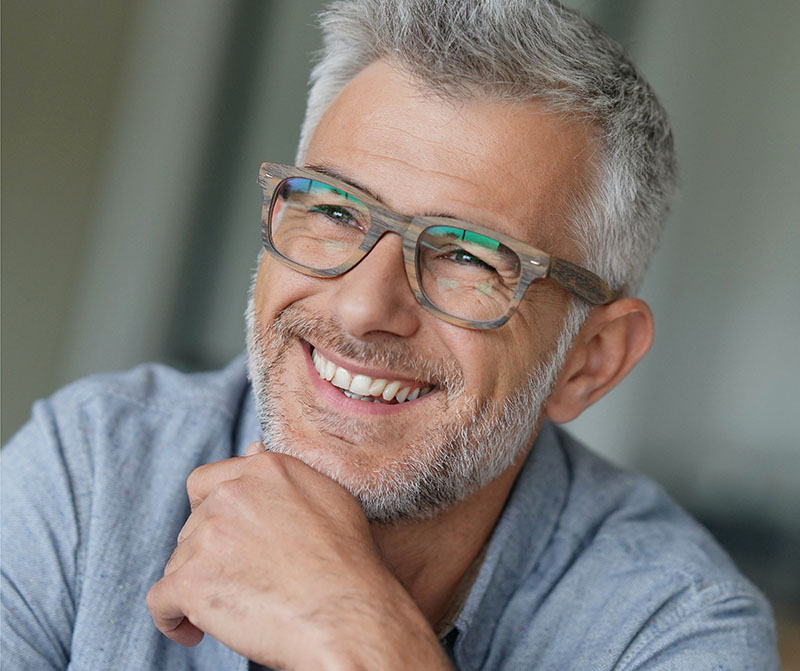 Man wearing glasses smiling with white teeth, resting his head on his hand