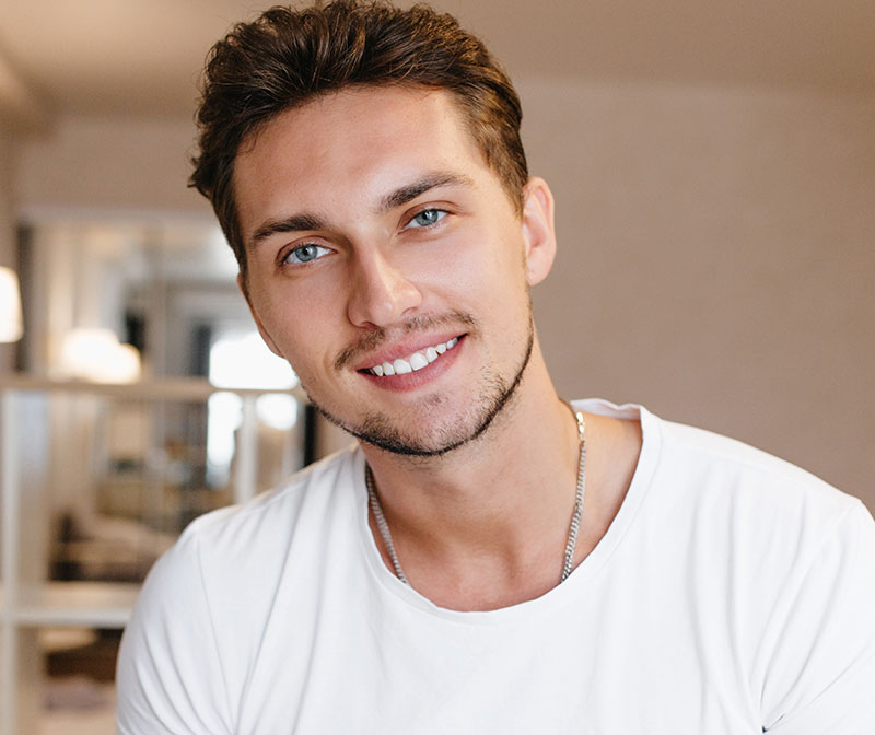 Man wearing a white t-shirt and chain smiling with white teeth