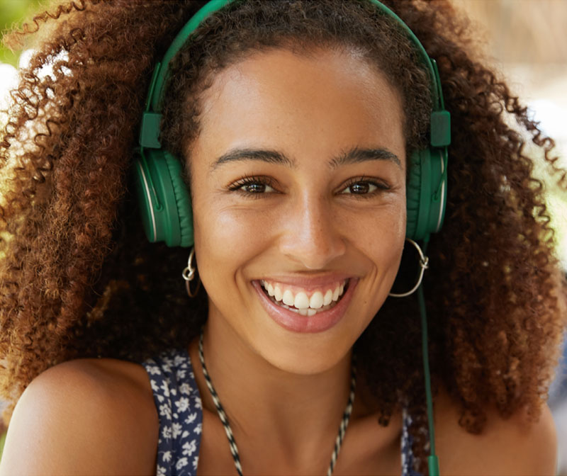 Woman wearing green headphones and a patterned top smiling